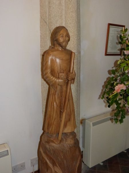 In Saint-Allen is de patroonheilige afgebeeld als monnik onderweg (reisstaf) met rozenkrans en gebedenboek of Bijbel.